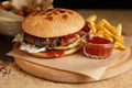 Big fat hamburger cooked on grill and served on wooden plate with fries and ketchup. Traditional American burger for dinner