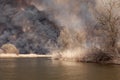 Big fire and black smoke on the other side of river. Field and dry grass are burning Royalty Free Stock Photo