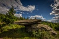 Big flat rock sitting on other on Obri Skaly with green grass, pine trees and dark blue cloudy sky under hill Serak in Jeseniky Royalty Free Stock Photo