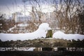 Big fluffy soft snowdrift on a wooden fence on snowy winter day with visible trees and modern buildings on the