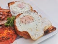 Big 2 fried eggs of English breakfast with sunny fried eggs, bacon, tomatos, ham on Turkish flat grilled bread on white dish