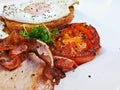 Big fried grilled tomato of English breakfast with sunny fried eggs, bacon, tomatos, ham on Turkish flat grilled bread on white Royalty Free Stock Photo