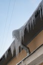 Big frozen icicles dangerously hanging from building edge on cold winter day. Ice dam on roof Royalty Free Stock Photo