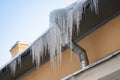 Big frozen icicles dangerously hanging from building edge on cold winter day. Ice dam on roof Royalty Free Stock Photo