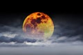 Big full yellow red moon in dark blue cloudy sky over some clouds. Royalty Free Stock Photo