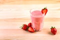 A big glass filled with an tasteful milkshake with a red strawberry on the top on a light brown wooden desk. Royalty Free Stock Photo