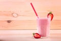 A big glass full of appetizing smoothie. A berry shake on a wooden background. Tasty milkshake with a straw and cut strawberries. Royalty Free Stock Photo