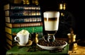 Big glass with latte stand in coffee beans. Atmosphere of library with old books around and grinder on dark background Royalty Free Stock Photo