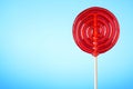 Big glossy red lollipop on wooden stick on blue background