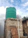 A big green water tank sits on a high vertical room built with bricks