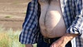 Big hairy belly of a man from under a plaid shirt. A male farmer stands in the field.