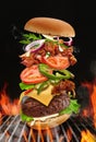 Big hamburger roasted on barbecue BBQ grill with bright flaming fire against black background. Beef cutlet, ham, cheese Royalty Free Stock Photo