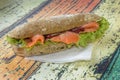 Big and hearty sandwich with red fish, salmon fillet, salad, cranberry and fresh bun. the concept of lunch. on a wooden colored ba