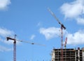 Big hoisting tower cranes and top section of modern construction building in a city over blue sky with clouds Royalty Free Stock Photo