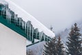 Big icicles and snow hanging over the rain gutter on a roof of a traditional wooden house in the mountains in winter. Royalty Free Stock Photo