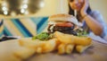 A big juicy burger with two cutlets, vegetables, sauce and french fries on the table in a cafe.