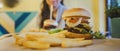 A big juicy burger with two cutlets, vegetables, sauce and french fries on the table in a cafe.