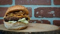 Big juicy hamburger with caramelized onions, cheddar cheese, french fries, lettuce on wooden tray with brick wall background Royalty Free Stock Photo