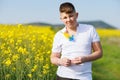 Teenage guy in T-shirt with Ukrainian flowers on it enjoys sun while standing in rapeseed field against clear sky Royalty Free Stock Photo