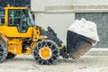 Big loader machine with steel metal chains removing big snow pile from city street at alpine mountain region in winter. Heavy