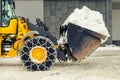 Big loader machine with steel metal chains removing big snow pile from city street at alpine mountain region in winter. Heavy