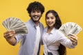 Big luck and win concept. Excited young indian couple holding dollar cash, posing with money on yellow background Royalty Free Stock Photo