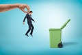 Big male hand throwing little businessman into green garbage bin on blue background