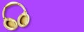 Big modern golden headphones isolated on bright purple background.