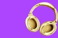 Big modern golden headphones isolated on bright purple background.