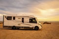 Big modern motorhome camper van parked on the ground and beautiful beach with sea and sunset lights in background. Concept of Royalty Free Stock Photo