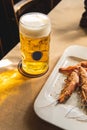 Big mug of fresh cold beer and fried tiger prawns on the table. A low-alcohol beverage and a snack are on the table. Light back Royalty Free Stock Photo