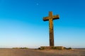 Big old Christian stone cross covered with bright yellow lichen in front of a clear blue sky at the beginning sunset