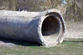 A big old gray concrete pipe lying on a green pipe outside