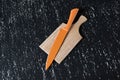 Big orange kitchen knife on wooden cutting board on black table. Royalty Free Stock Photo