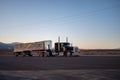 Big Peterbilt long nose truck with a large trailer driving on the deserted roads at sunset