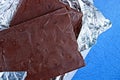 Pieces of brown chocolate in gray foil on a blue table