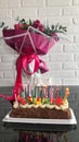 Big pink beautiful festive gift bouquet of flowers for a birthday and a cake with burning candles on the table against the Royalty Free Stock Photo