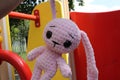 Big pink hare on the playground. Hare in the hands of an unrecognizable girl. The knitted hare went out for a walk