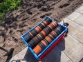 Big plastic box full with empty brown and black plastic pots stacked together for plants with flower bed in the background in Royalty Free Stock Photo