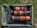 Big plastic box full with empty brown and black plastic pots stacked together for plants with flower bed in the background in Royalty Free Stock Photo