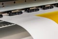 Big professional printer, processing a large scale glossy sheet of yellow paper rolls for color sampling.