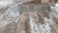 Big puddle with dirty melting snow and blurry reflection of old building with two windows. Road in thaw season. Grunge textures. Royalty Free Stock Photo