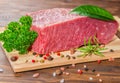 big raw boneless beef meat with pepper, rosemary, parsley, laurel, salt on wooden table, close up