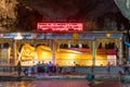Big reclining golden Buddha inside a temple cave with stalactites. Buddha surrounded by neon lights. People praying and bringing