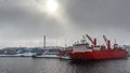 Big red cargo ship under the dull arctic sun and heavy snowfall in the port of Aasiaat, with village in the background, Greenland