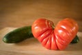 Big red heart-shaped tomato and cucumber on a wooden plate Royalty Free Stock Photo