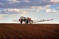 Red sprayer with long arms at the arable field makes fertilizers in early spring view with clouds Royalty Free Stock Photo