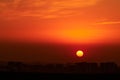 A big red sun in the sunset sky over the roofs of buildings, urban landscape. Evening sky in bright sunlight over the twilight Royalty Free Stock Photo