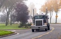 Dark big rig classic semi truck with high pipes turning on the autumn road with fog Royalty Free Stock Photo