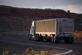 Big rig semi truck with bulk covered semi trailer going on winding road with red rocks of Arizona landscape in twilight